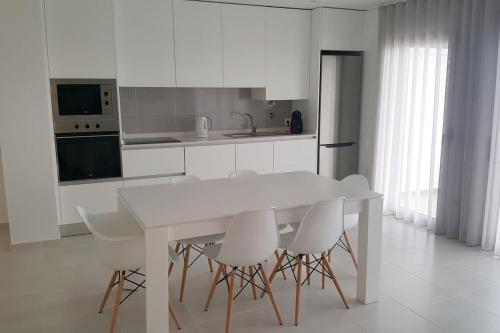 a white kitchen with a white table and chairs at Marnix´s Apartment in Nazaré