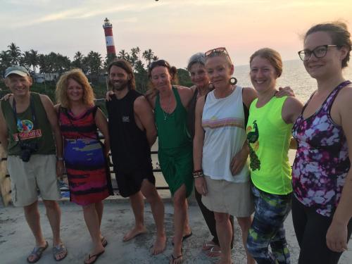 a group of people standing on the beach with a lighthouse in the background at The Ocean Park Beach Resort in Kovalam