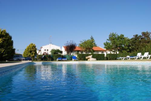 a swimming pool with blue water and two white chairs at Apartamentos Vale Da Varzea in Areia Branca