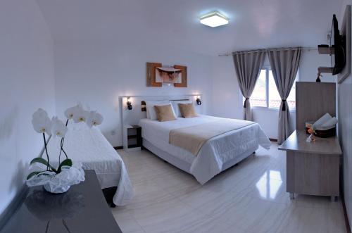 a white bedroom with a bed and a table at La Plage Residence in Garopaba