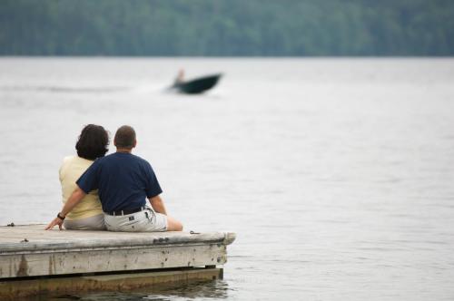 a man and woman sitting on a dock looking at the water at Auberge du Lac-à-l'Eau-Claire in Saint-Alexis-des-Monts