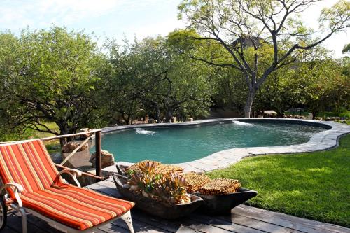 a swimming pool with a rocking chair and a chair at Toshari Lodge in Okaukuejo