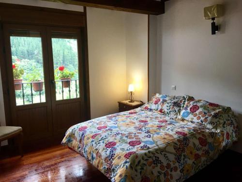 a bedroom with a bed with a floral bedspread and a window at La Casuca de Pumareña in Pumareña