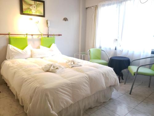 a bedroom with a large white bed with green chairs at Noria Hotel in Villa Carlos Paz