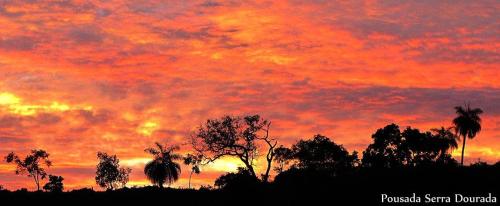 a sunset with palm trees in the foreground at Pousada Serra Dourada in Goiás