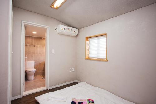 baño con cama, aseo y ventana en Bookmark Guesthouse en Seogwipo