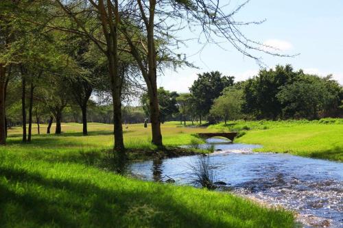 a river in a field with trees and a bridge at Kili Villa Kilimanjaro Luxury Retreat in Arusha