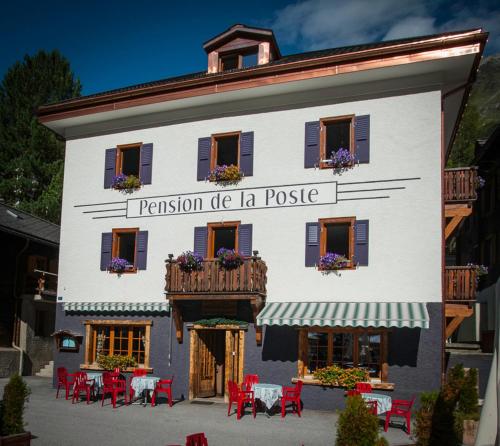 a white building with a balcony and tables and chairs at Pension de la Poste in Zinal