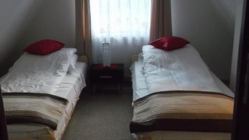 two beds with red pillows sitting next to a window at Apartamenty Lejówka in Chochołów