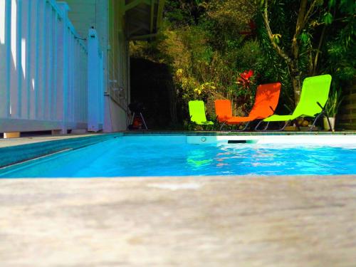 a swimming pool with green and orange chairs next to it at La Villa du soleil in Les Trois-Îlets