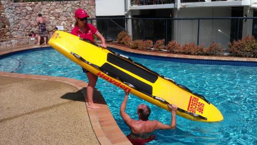 a woman holding a yellow paddle board in a swimming pool at The Beach Retreat Coolum in Coolum Beach