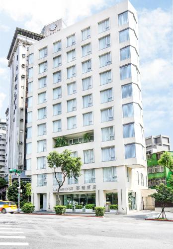 a white building with a tree in front of it at Ambience Hotel Taipei in Taipei