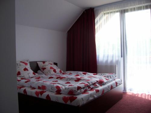 a bedroom with a bed with red and white sheets and a window at Pensiunea Mara in Deseşti
