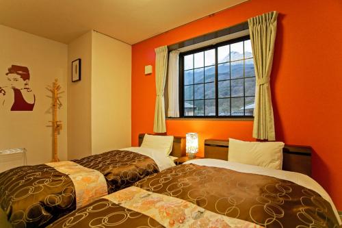 由布市にある和モダンな温泉旅館　湯布院旅の蔵のオレンジ色の壁と窓が備わる客室で、ベッド2台が付いています。