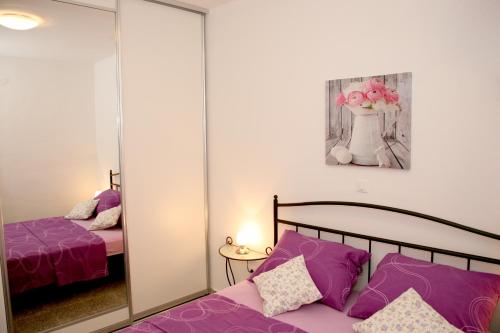 Schlafzimmer mit einem Bett mit lila Kissen und einem Spiegel in der Unterkunft Apartments Bašić in Split