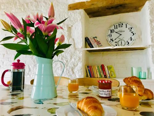 a table with a vase of flowers and croissants and a clock at La Blatière French Cottages in La Chapelle-Saint-Étienne