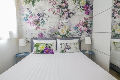 a white bed with two pillows and a floral wall at Charming and cosy apartment in Bologna