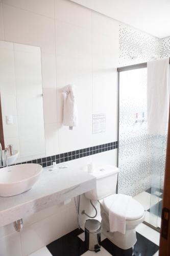 a white bathroom with a sink and a toilet at Grand Enio Hotel e Cantina in Varginha