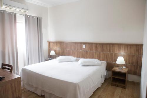 a bedroom with a large white bed with two lamps at Grand Enio Hotel e Cantina in Varginha