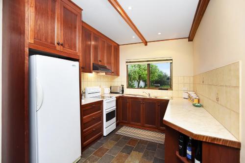 - une cuisine avec des placards en bois et un réfrigérateur blanc dans l'établissement Don Carmella - Aldinga Beach - C21 SouthCoast Holidays, à Aldinga Beach