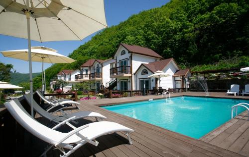 a swimming pool with chairs and an umbrella at Forest of Color Pension in Hongcheon