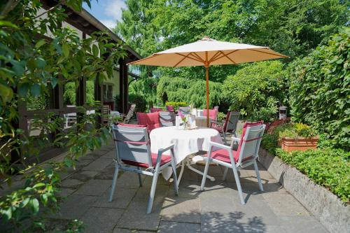 a table and chairs with an umbrella on a patio at Romantik Waldhotel Mangold in Bergisch Gladbach
