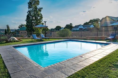 a swimming pool with two chairs and an umbrella at Kyalami Creek in Midrand