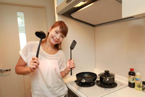 a woman holding two utensils in a kitchen at IBASHO ShibuyaDogenzaka803 in Tokyo