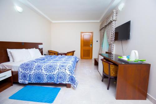Schlafzimmer mit einem Bett, einem Schreibtisch und einem TV in der Unterkunft Monarch Hotel in Accra