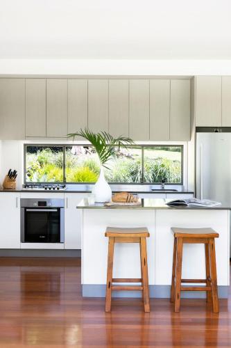 a kitchen with white cabinets and two wooden stools at Lily Pad at Byron Bay in Byron Bay