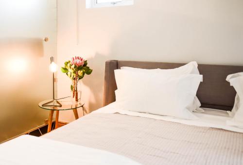 un letto con lenzuola bianche e un vaso di fiori su un tavolo di Collection Luxury Accommodation 7 on Murray unit 1 a Stellenbosch