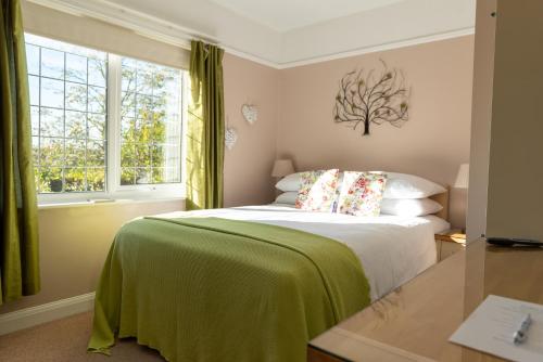 a bedroom with a bed with a green blanket and two windows at Armeria in Wells next the Sea