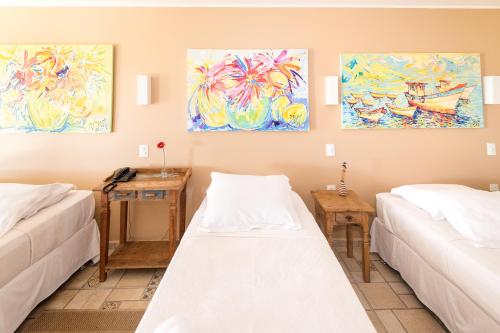 two beds in a room with paintings on the wall at Pousada La Dolce Vita in Búzios