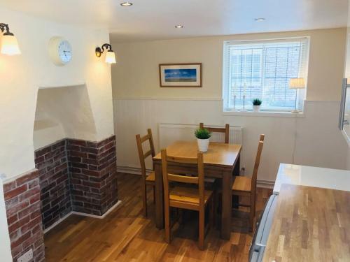 a dining room with a table and a brick fireplace at Wisteria Cottage in Gravesend