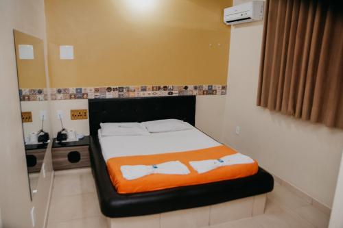 a bed in a small room with an orange blanket on it at Hotel Positano in Taguatinga