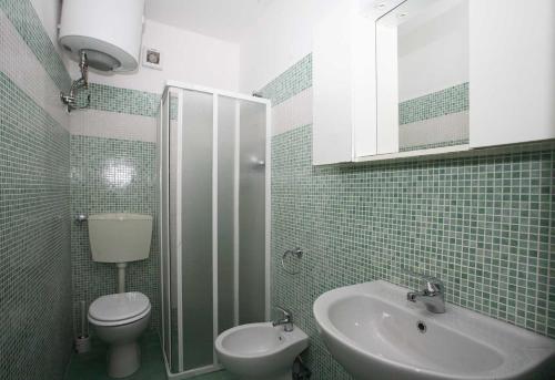 a green tiled bathroom with a toilet and a sink at Solarium/piscina in Bibione