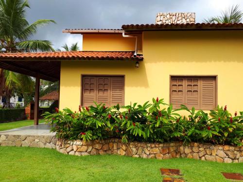 a yellow house with brown doors and a stone wall at Casa de Praia em Carneiros in Tamandaré