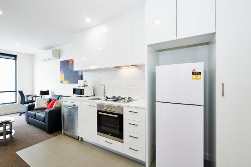 a kitchen with white appliances and a living room at Melbourne Knox Central Apartment Hotel Official in Wantirna