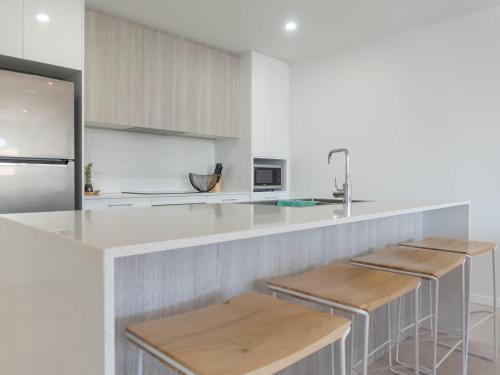 a kitchen with a white counter and wooden stools at Rockpools 1 in Sawtell
