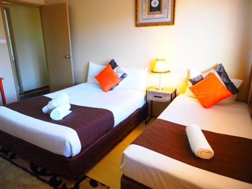 two beds in a hotel room with orange and white pillows at Bella Vista Motel in Gosford