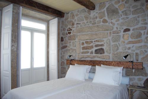 1 dormitorio con pared de piedra y 1 cama con sábanas blancas en Casa Dos Caldeireiros, en Oporto