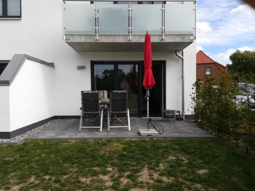 un patio con 2 sillas y una sombrilla roja en Haus Baltic Cube, en Börgerende-Rethwisch