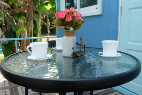 a glass table with two cups and a vase with flowers at Saengcha Farm Resort in Prachin Buri