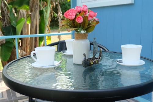 a table with two cups and a vase with pink roses at Saengcha Farm Resort in Prachin Buri