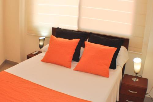 ein Bett mit orangefarbenen und schwarzen Kissen darauf in der Unterkunft Garzota Suites Airport in Guayaquil