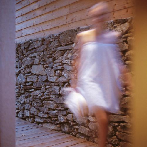 a woman in a white dress walking past a stone wall at Ferienpension Senfter in Innervillgraten