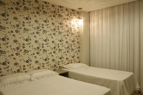 two beds in a room with floral wallpaper at 3qtos Quadra do Mar Lindo! in Guarapari