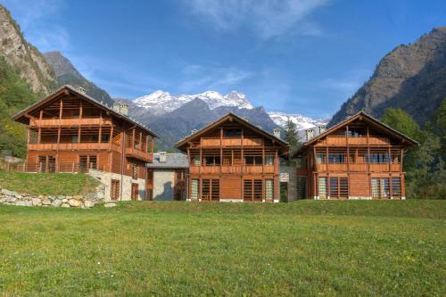 two large wooden buildings in a field with mountains at Pietre Gemelle Resort in Alagna Valsesia