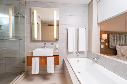 W łazience znajduje się umywalka, wanna i lustro. w obiekcie aha Harbour Bridge Hotel & Suites w Kapsztadzie