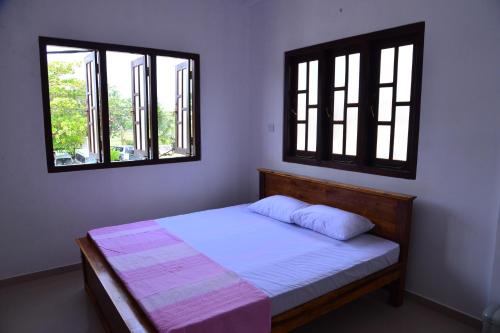 ein Schlafzimmer mit einem Bett und zwei Fenstern in der Unterkunft Roshan's Guest House in Hikkaduwa